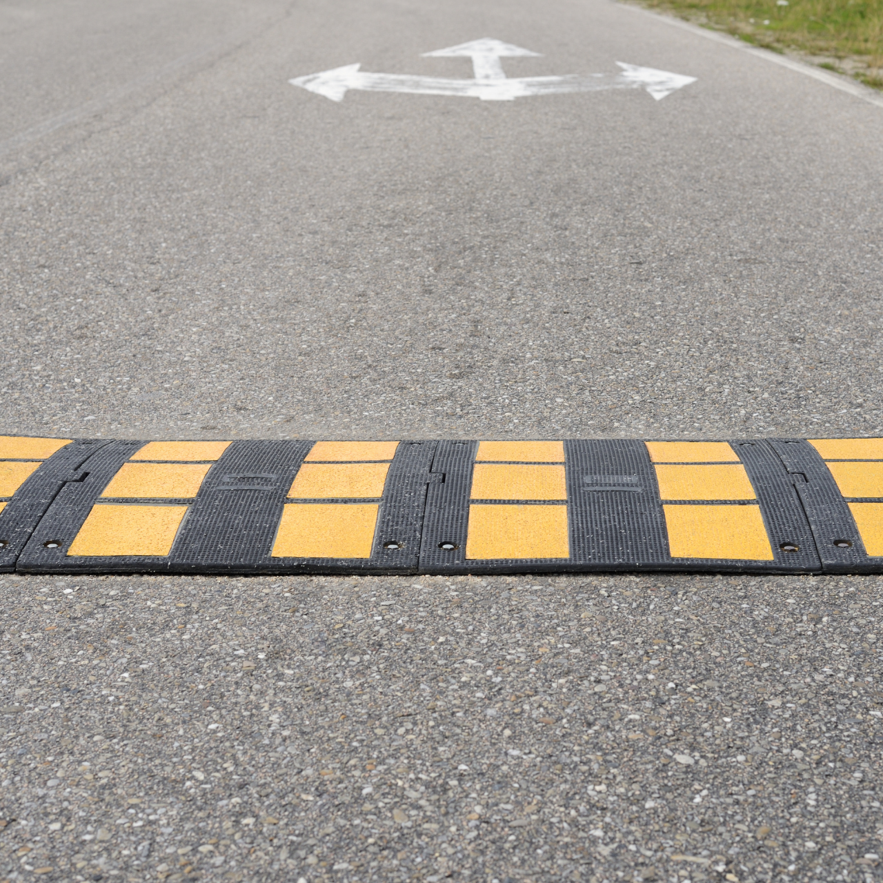 Speed bump painted with yellow and black stripes on a gray road with painted turn arrows.