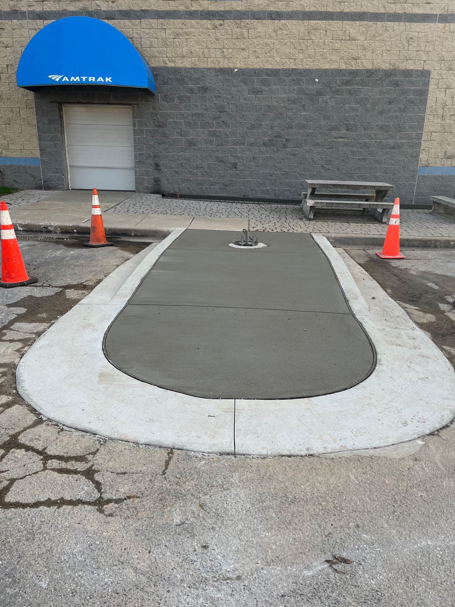 Freshly poured concrete pad with a curved border, in front of a building.
