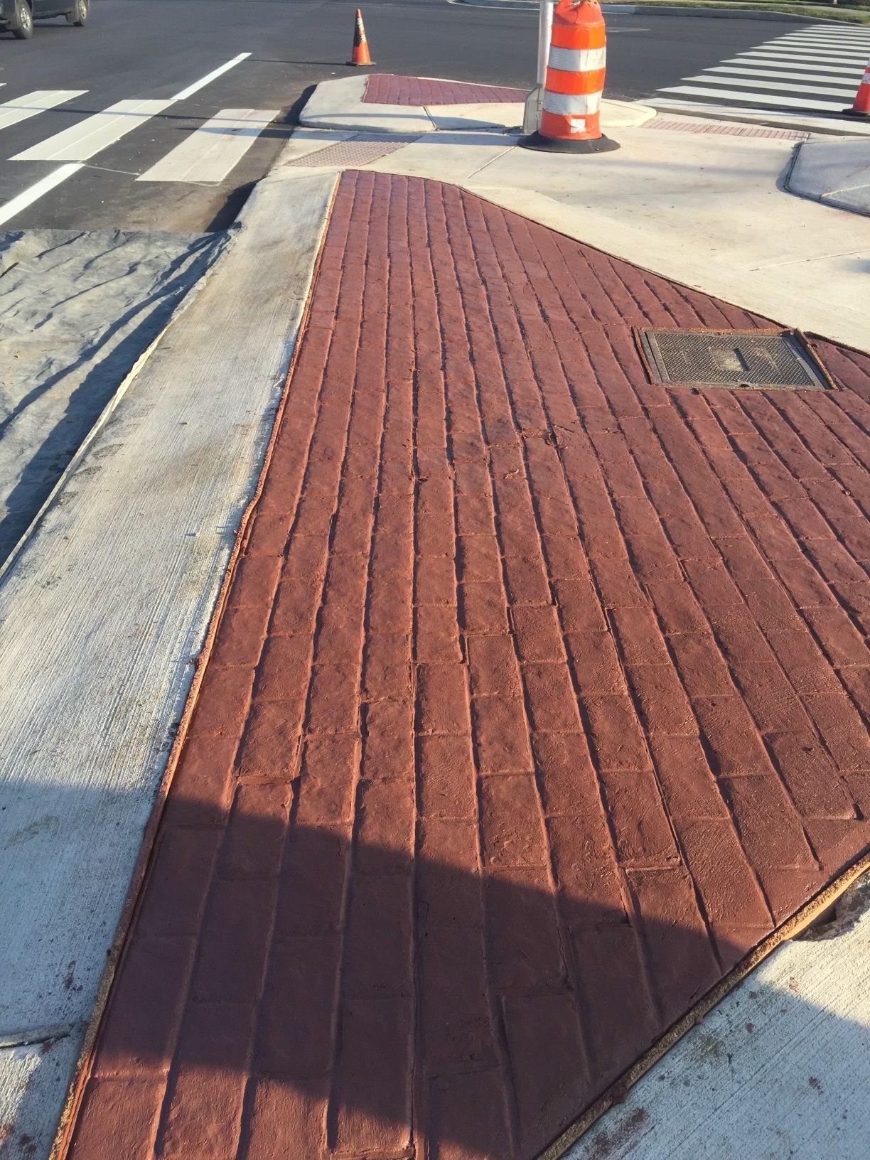 Red brick sidewalk angled toward a street, with white crosswalk lines and orange construction cones visible.