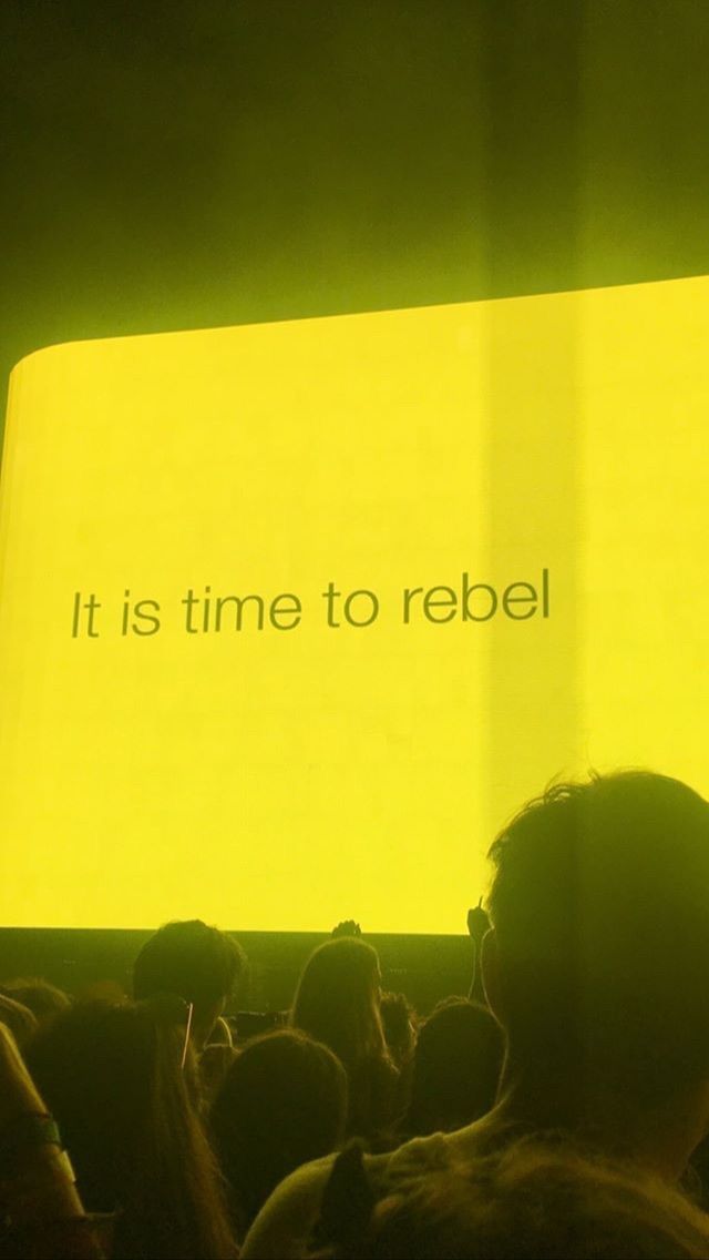 A group of people sitting in front of a yellow screen that says `` it is time to rebel ''.