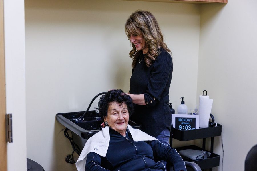 A professional stylist washes the hair of a person seated in a salon sink chair.