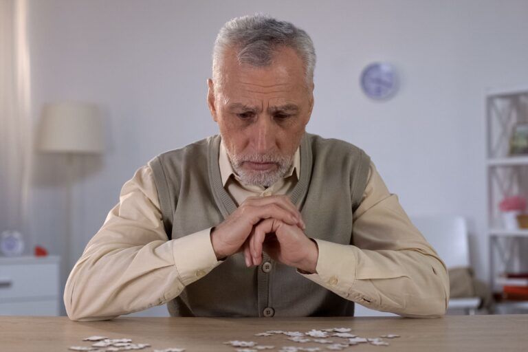 A person with a worried expression sits at a table, looking down at a small pile of coins.