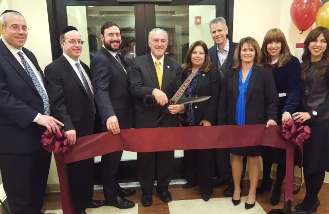A group of people in business attire performs a ribbon-cutting ceremony in front of a building entrance.