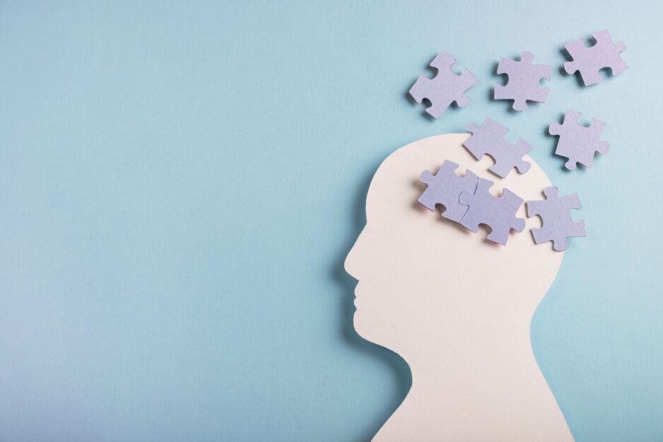 A white paper silhouette of a human head on a blue background, with jigsaw pieces forming and floating above the brain.