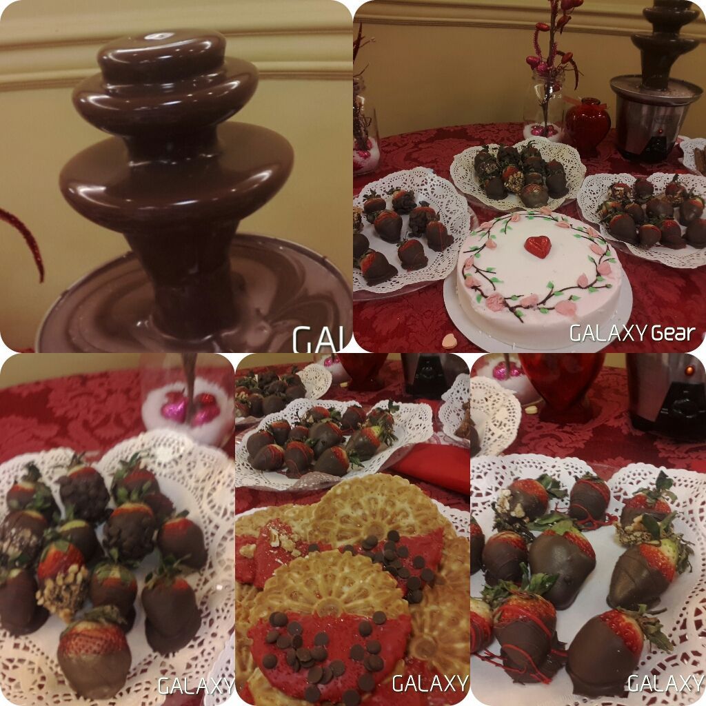 A dessert display featuring a chocolate fountain, plates of chocolate-covered strawberries, and a heart-decorated cake.