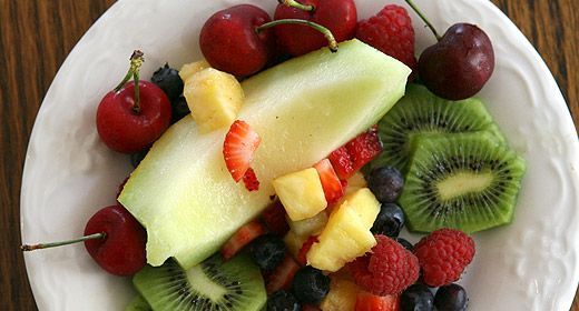 A white plate topped with sliced fruit and berries on a wooden table.