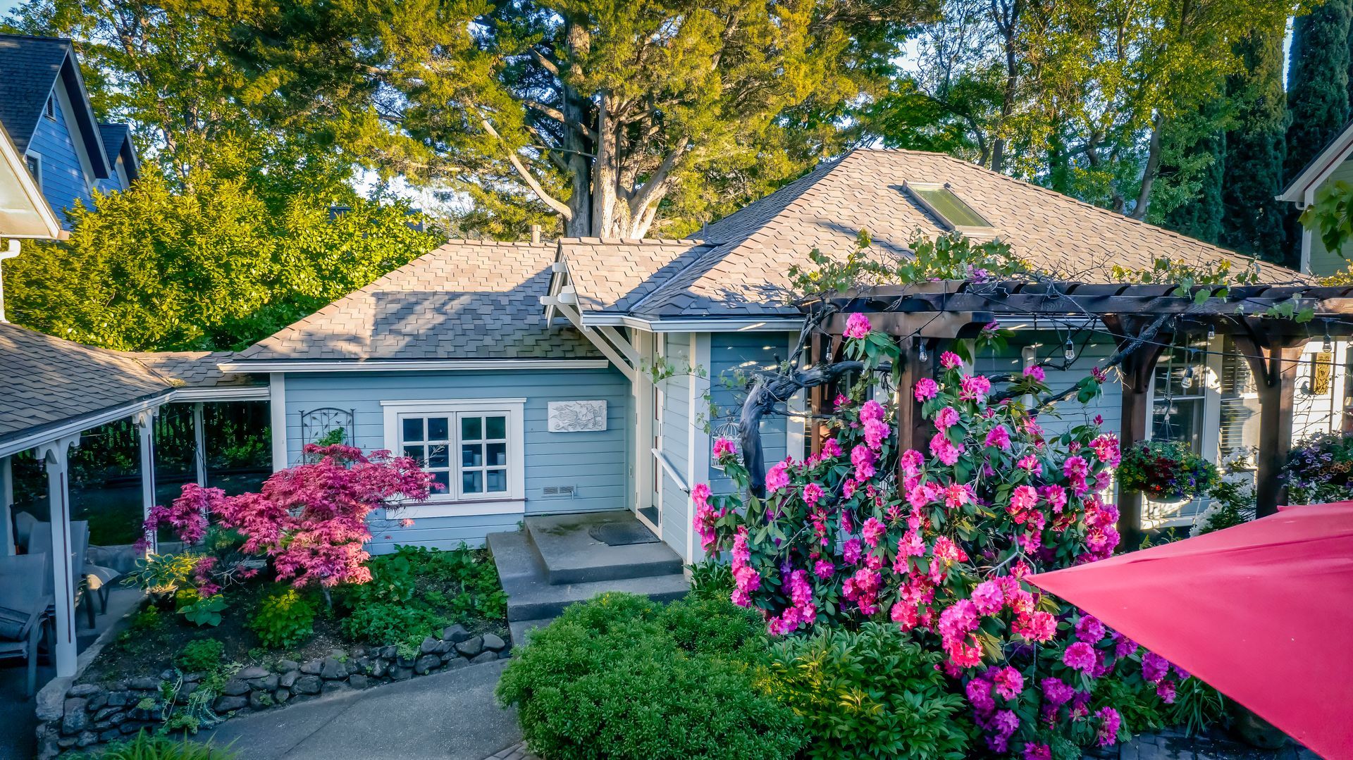 A small house with pink flowers and a red umbrella in front of it.