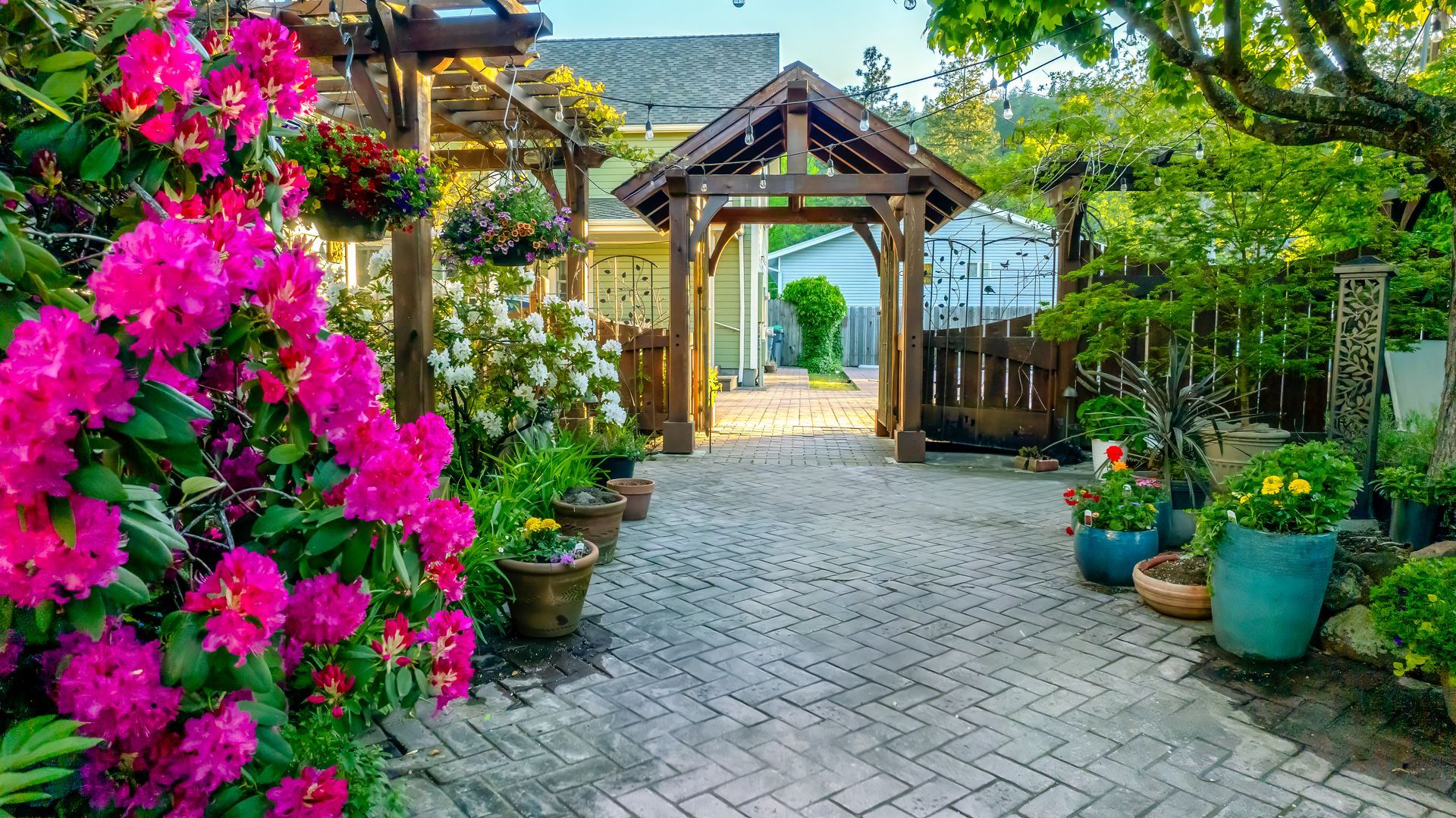 A brick walkway surrounded by potted plants and flowers leading to a house.