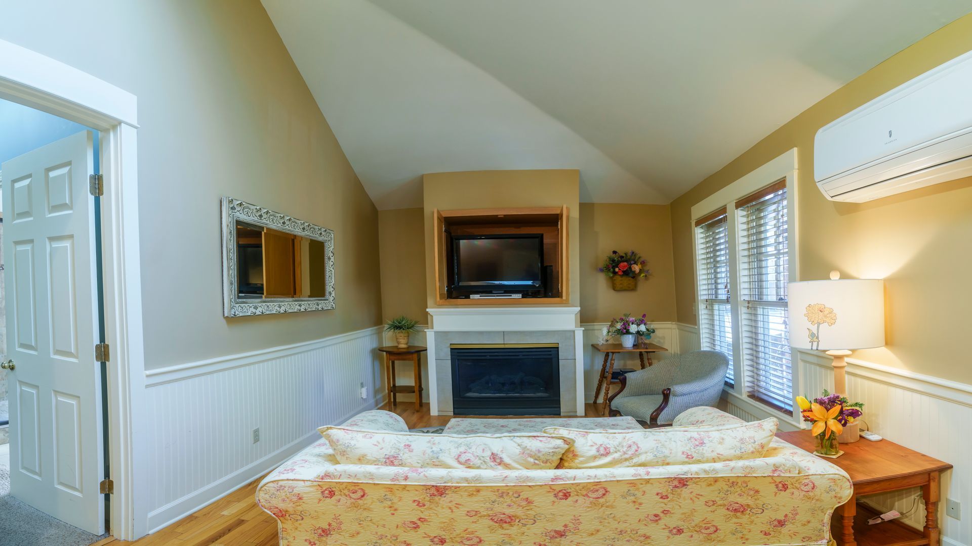 A living room with a couch , fireplace , television and air conditioner.