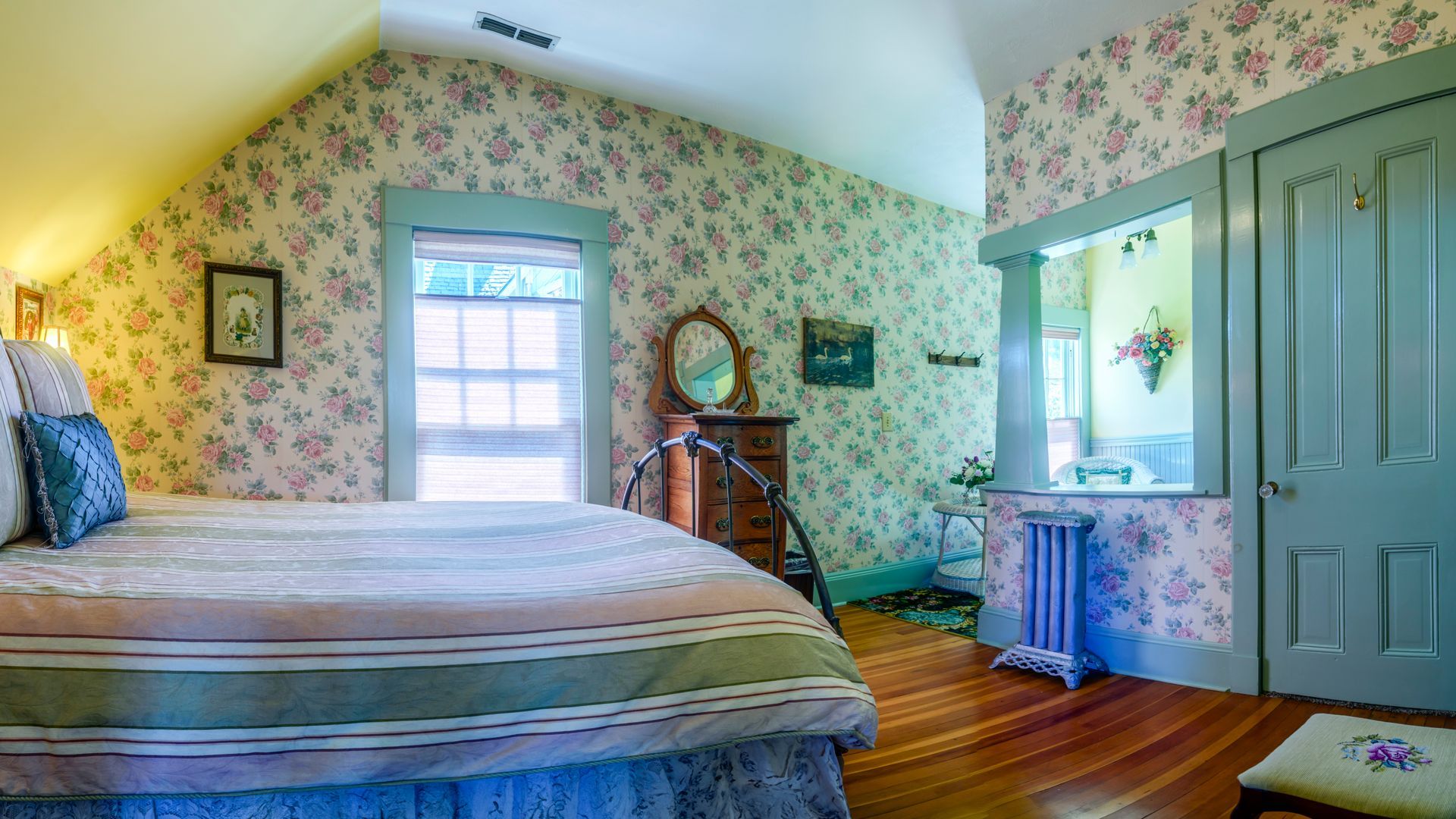 A bedroom with a bed , dresser , mirror and floral wallpaper.