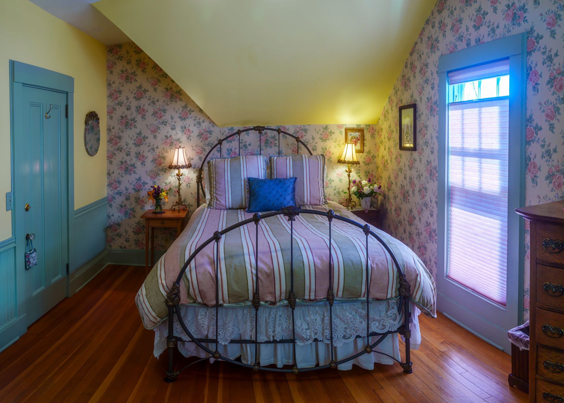 A bedroom with a bed , dresser , lamps and a window.