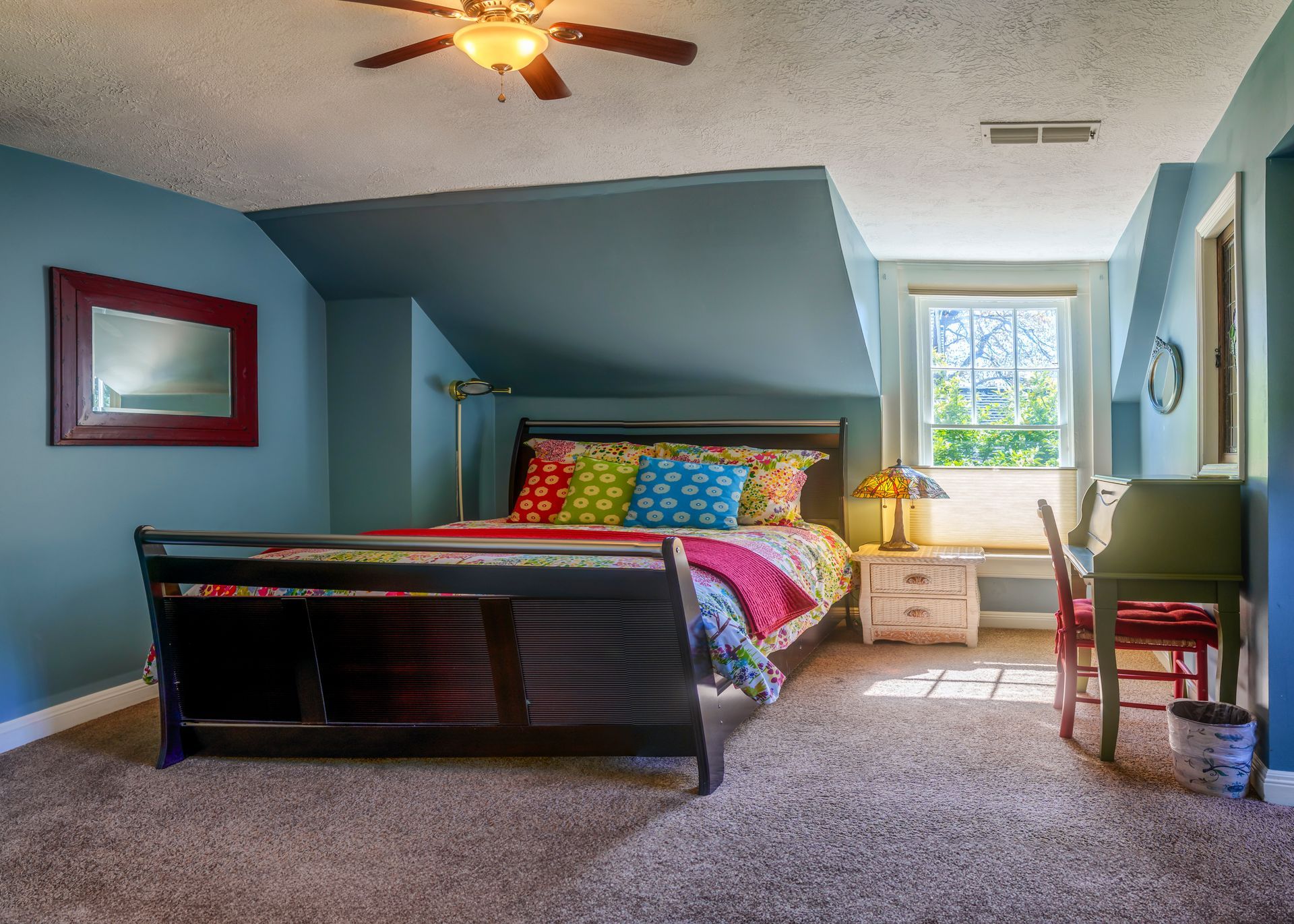 A bedroom with a bed , desk , mirror and ceiling fan.