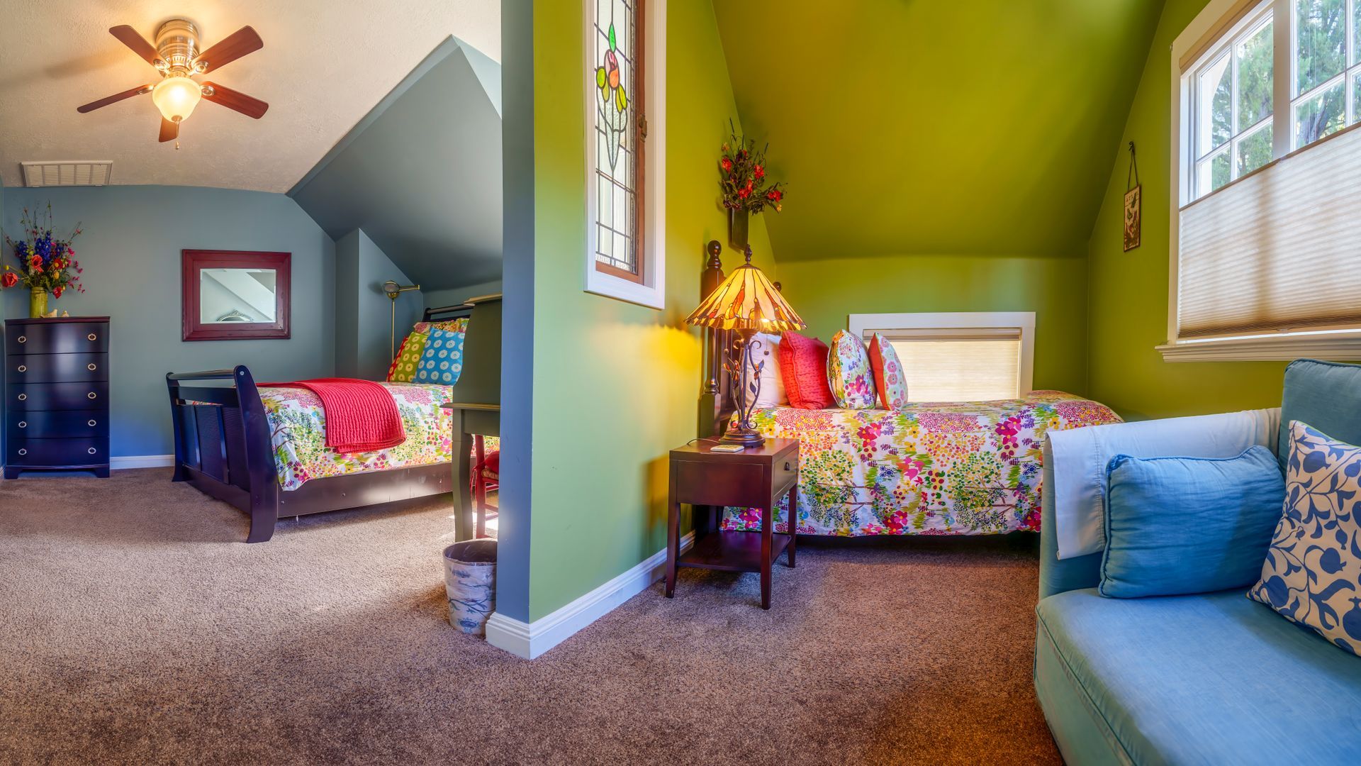 A bedroom with green walls , a bed , a couch , and a ceiling fan.