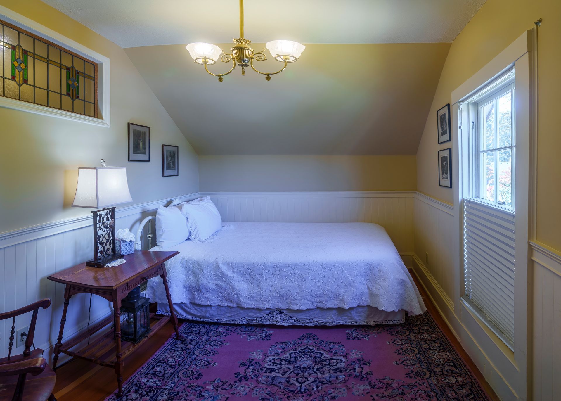 A bedroom with a bed , table , chair and window.