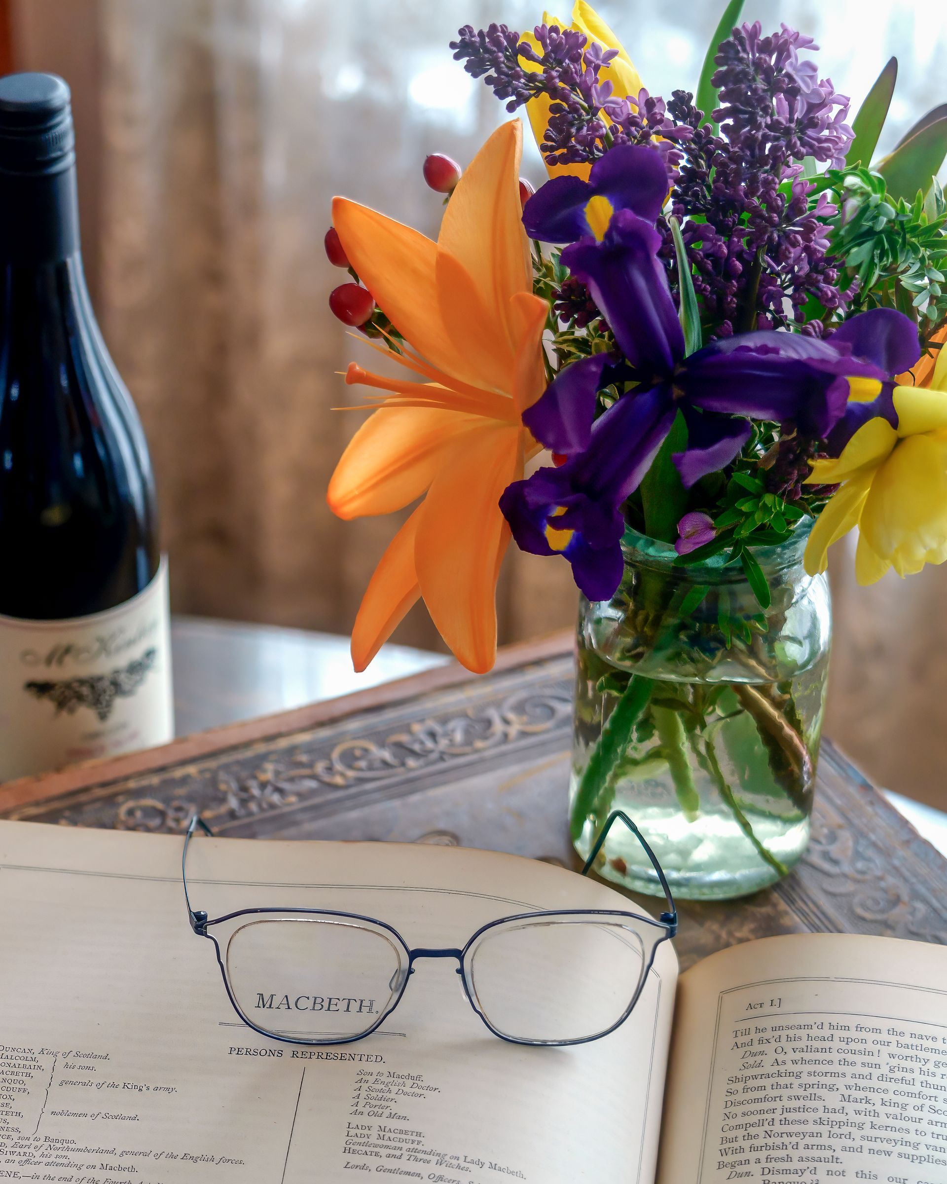 A pair of glasses sits on an open book next to a vase of flowers