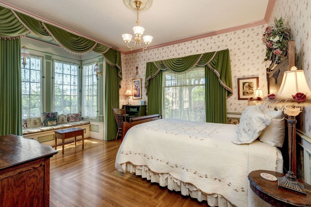 A bedroom with a bed , dresser , lamps , and a window seat.