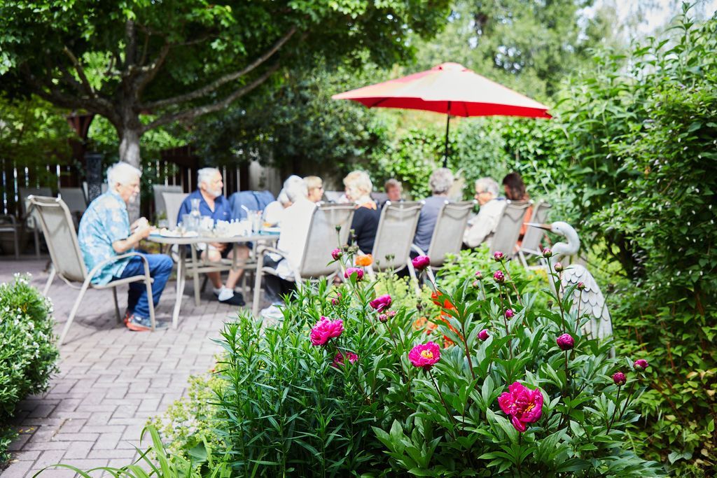 A group of people are sitting at a table under an umbrella in a garden.