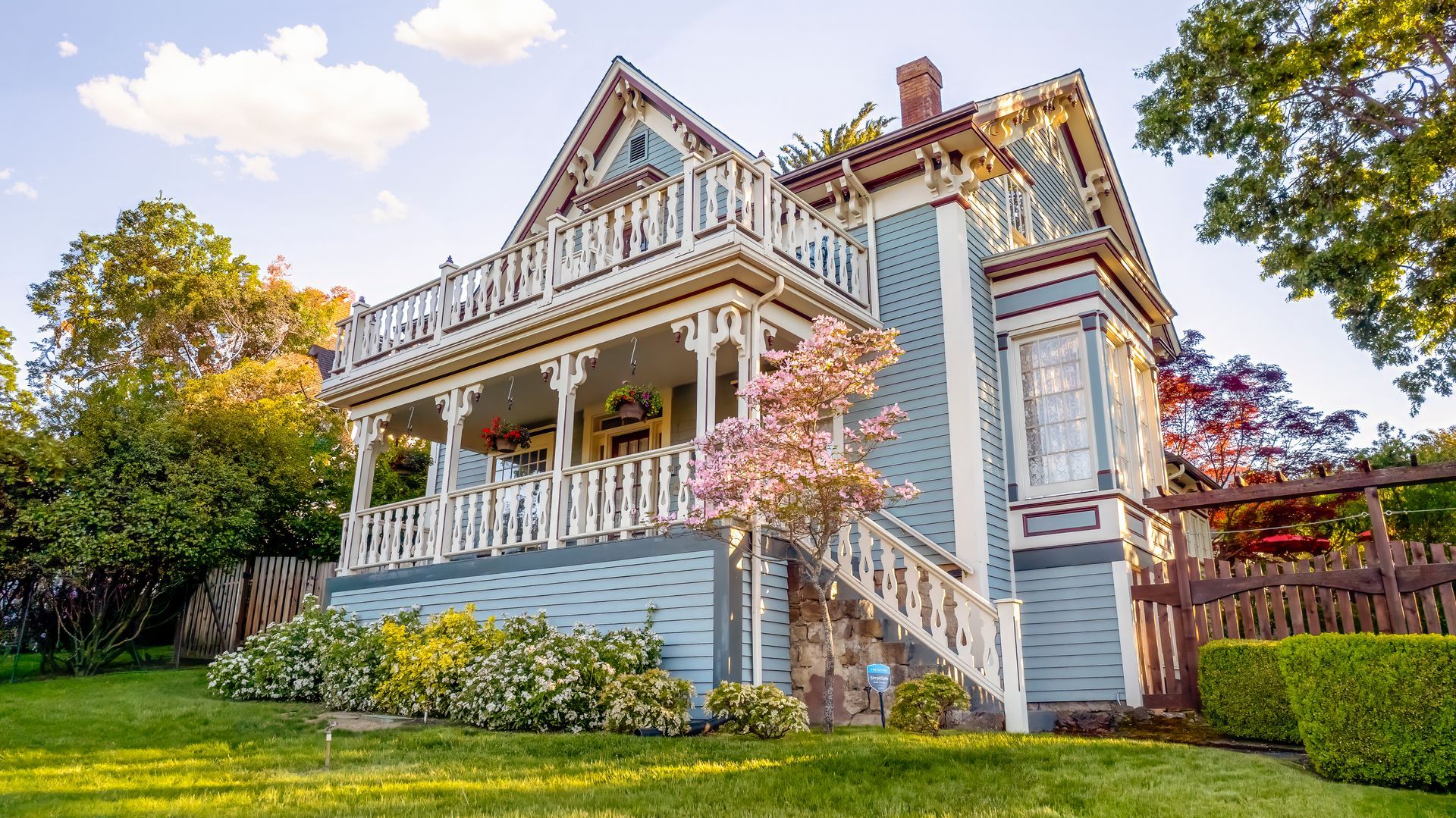 A large blue and white house with a large porch is sitting on top of a lush green lawn.