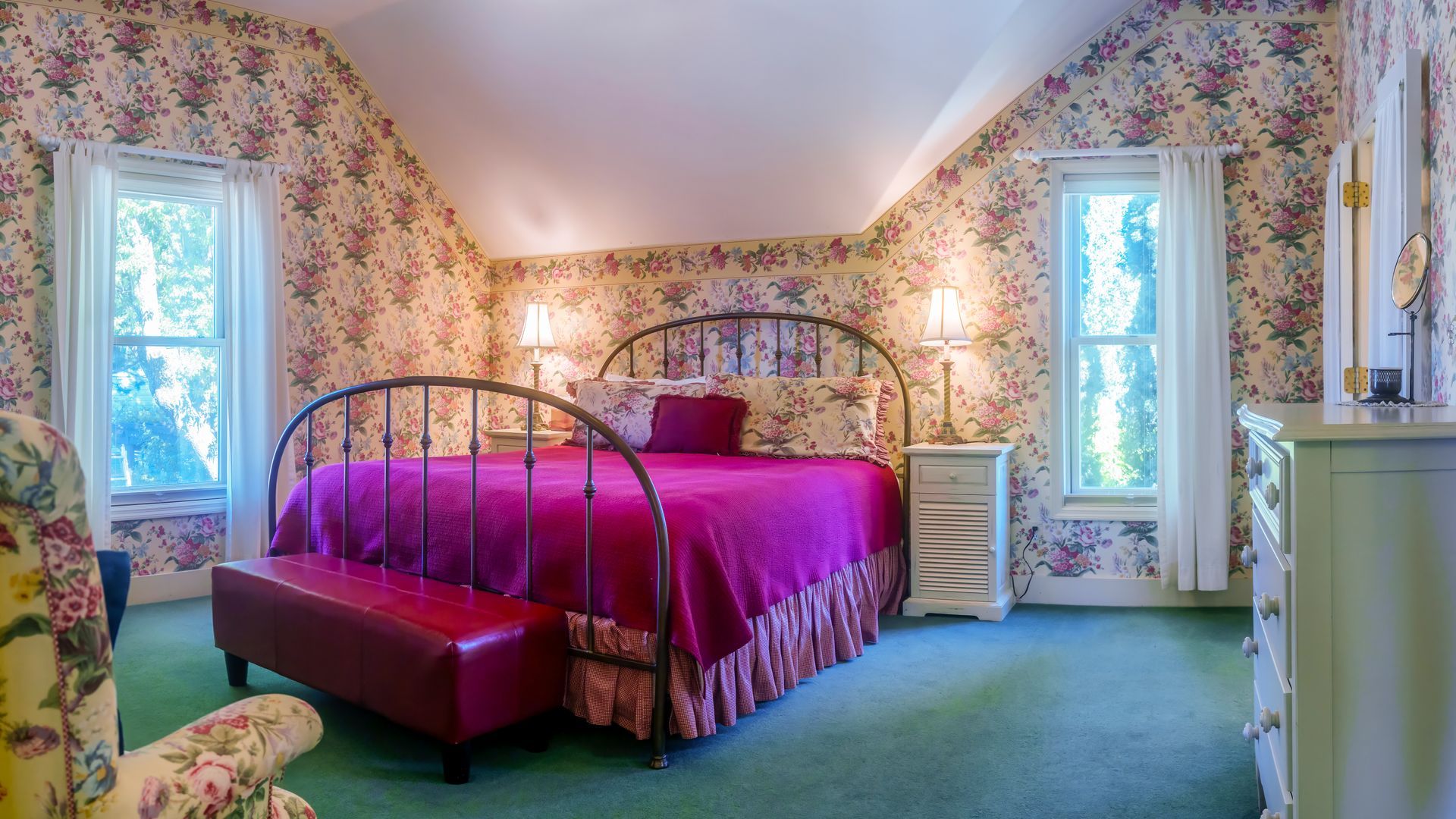 A bedroom with a bed , dresser , chair and floral wallpaper.