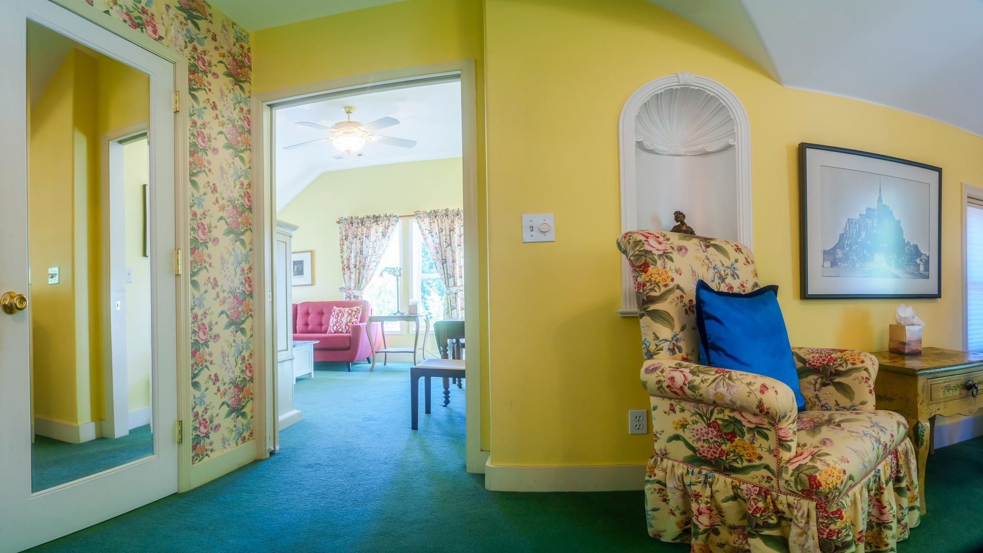 A living room with yellow walls , green carpet and a floral chair.