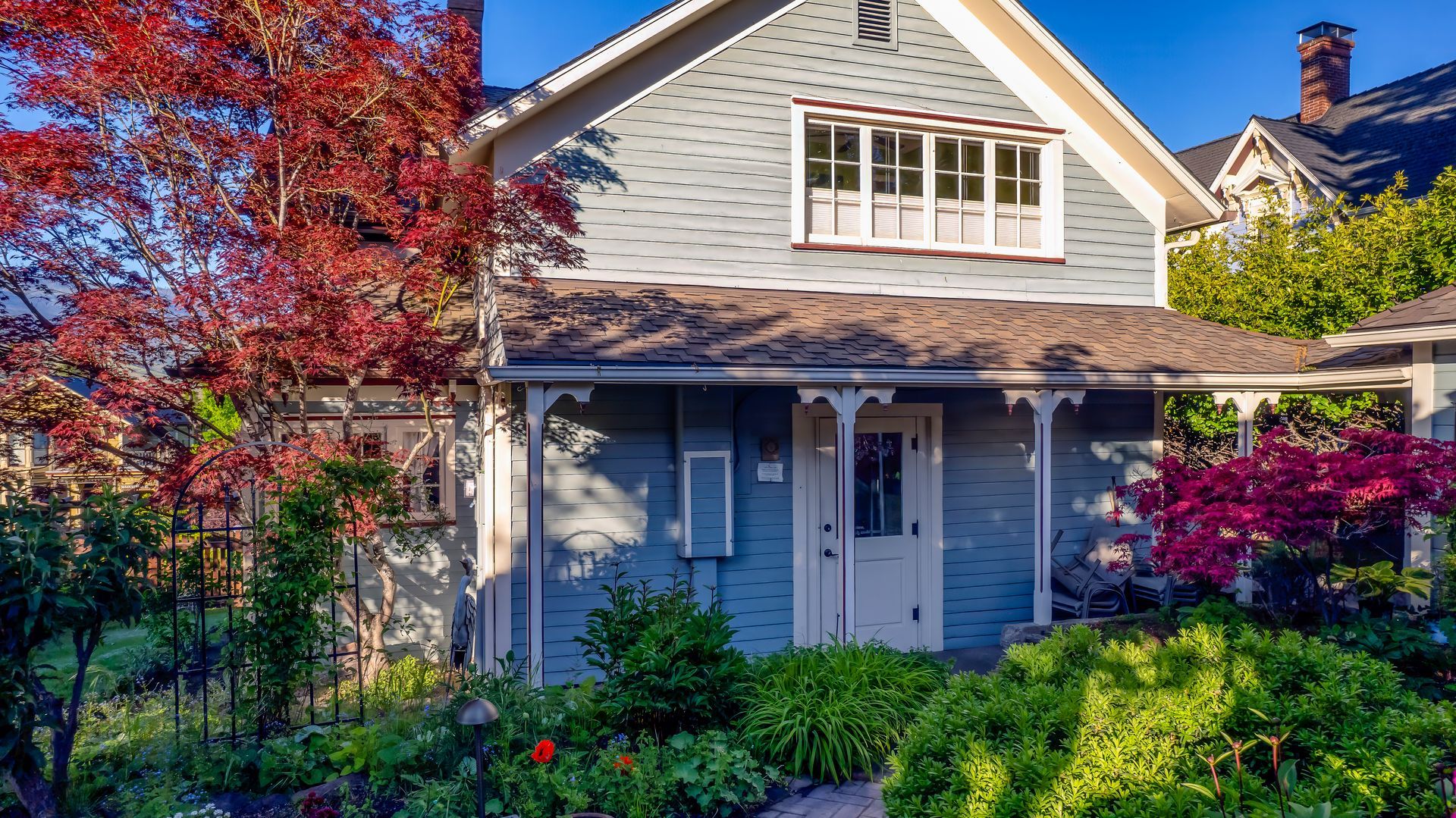 A blue house with a porch and flowers in front of it