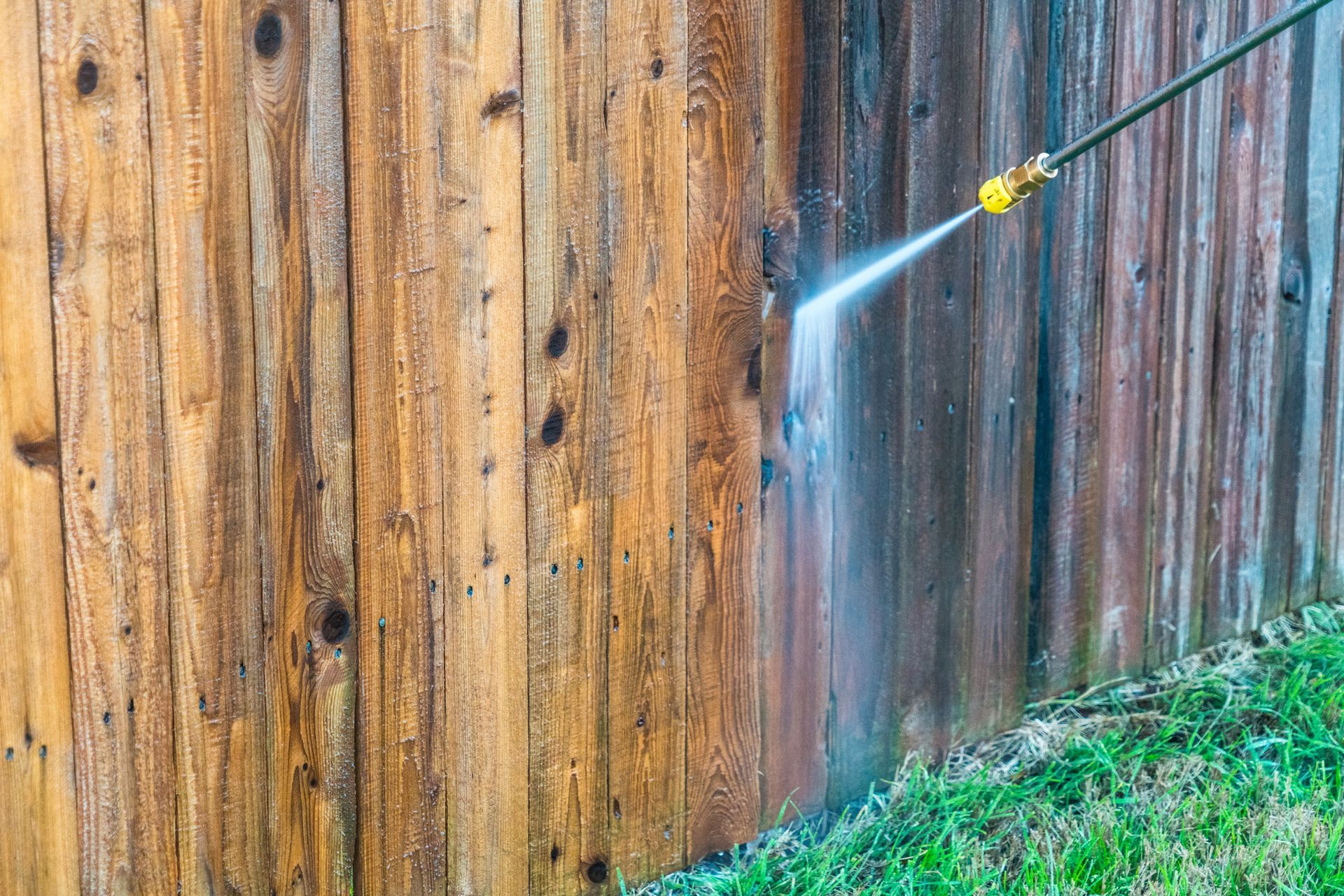 A person is using a high pressure washer to clean a wooden fence.