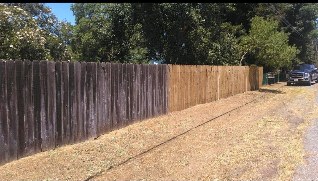 A person is using a high pressure washer to clean a wooden fence.