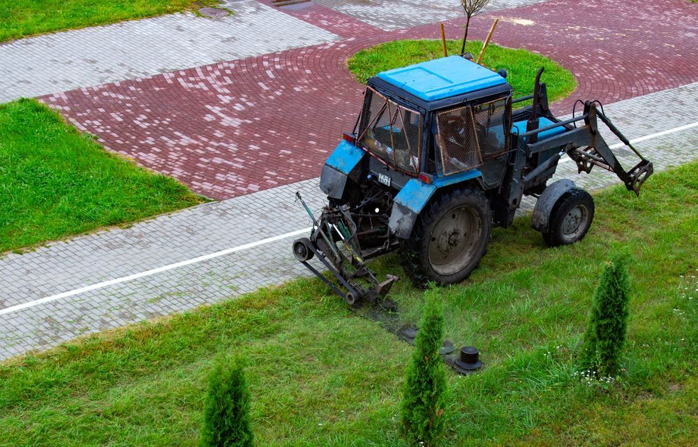 Blue Tractor Mowing Grass Next to a Brick Walkway and Green Space — Slash Mulch Co in Googa Creek, QLD