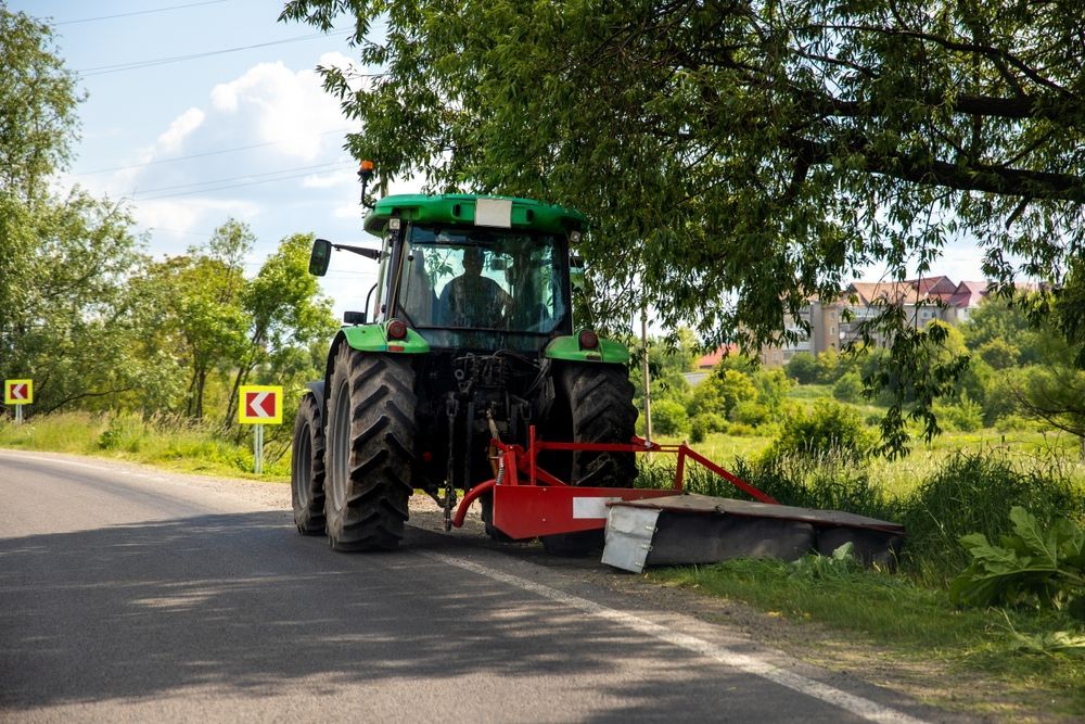 Green Tractor Mowing Roadside Grass on a Sunny Day — Slash Mulch Co in Googa Creek, QLD