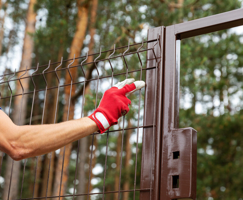 Hand in Red Glove Holding a Brown Wire Fence Next to a Brown Gate — Slash Mulch Co in Googa Creek, QLD