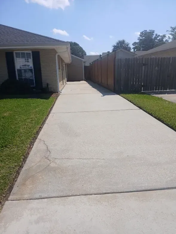 A concrete driveway leading alongside a beige house toward a wooden fence on a sunny day.