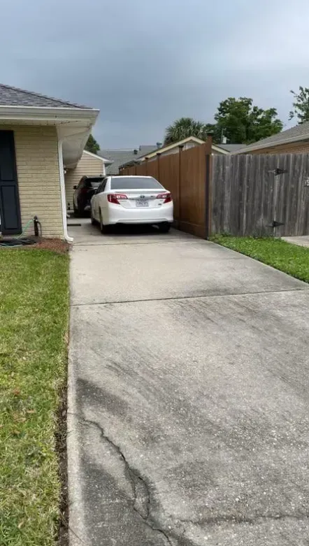 A white sedan parked on a residential concrete driveway next to a tan house and wooden privacy fence.