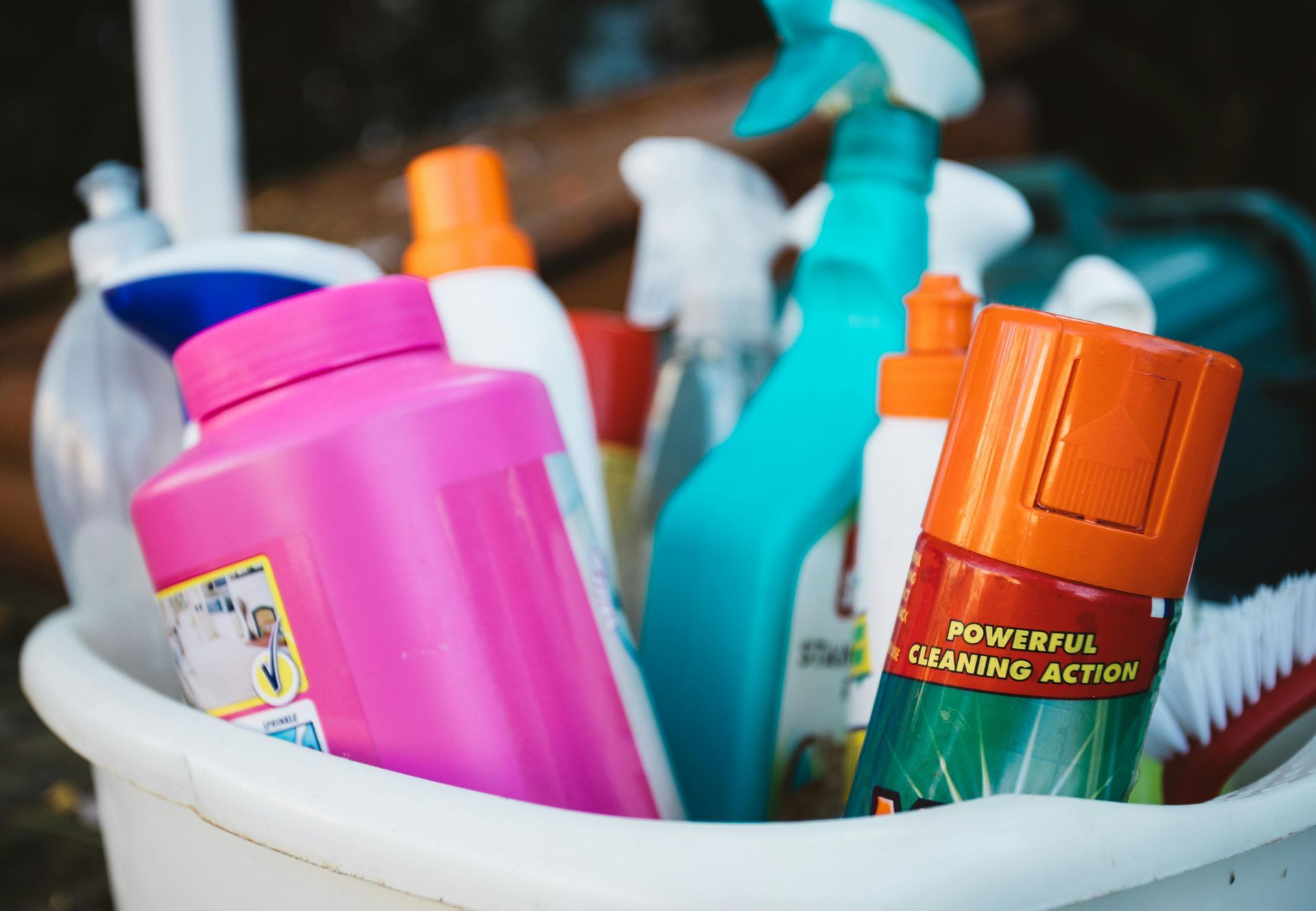 Assorted colorful cleaning bottles in a white bucket