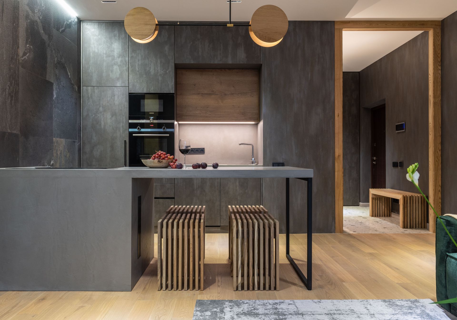Modern kitchen with gray cabinetry, black island, wooden stools, and warm pendant lights in a minimalist interior