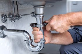 Hands tightening a chrome sink drain pipe under a bathroom sink