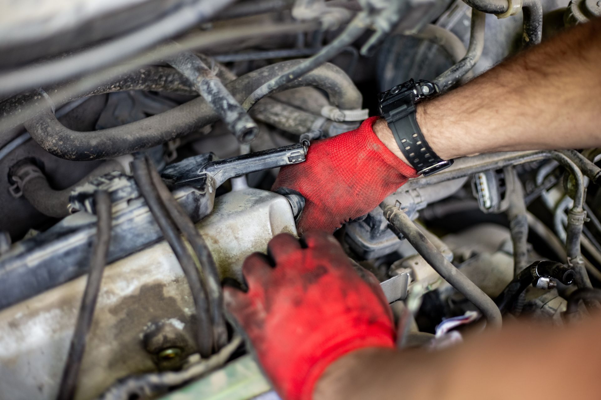 Gloved hands working on a car engine among tangled hoses and wires