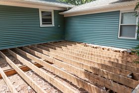 House foundation exposed with wooden floor joists visible beneath teal siding and windows