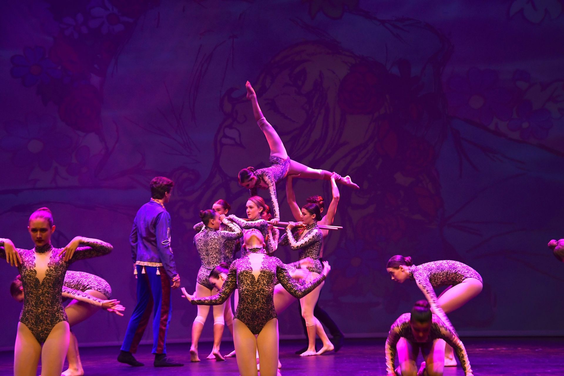 A group of dancers are performing on a stage with purple lights.