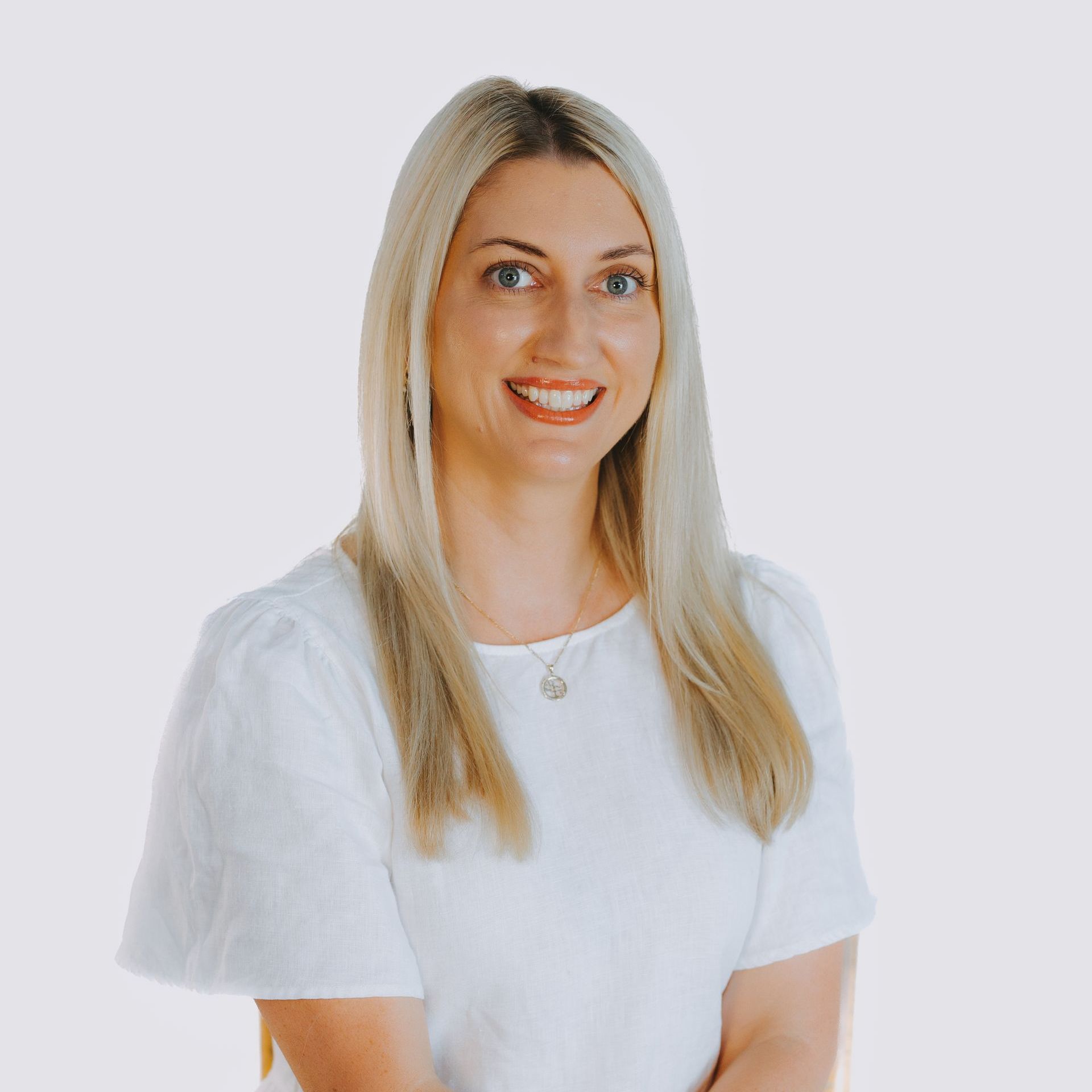 A woman wearing a white shirt and a necklace is smiling for the camera.