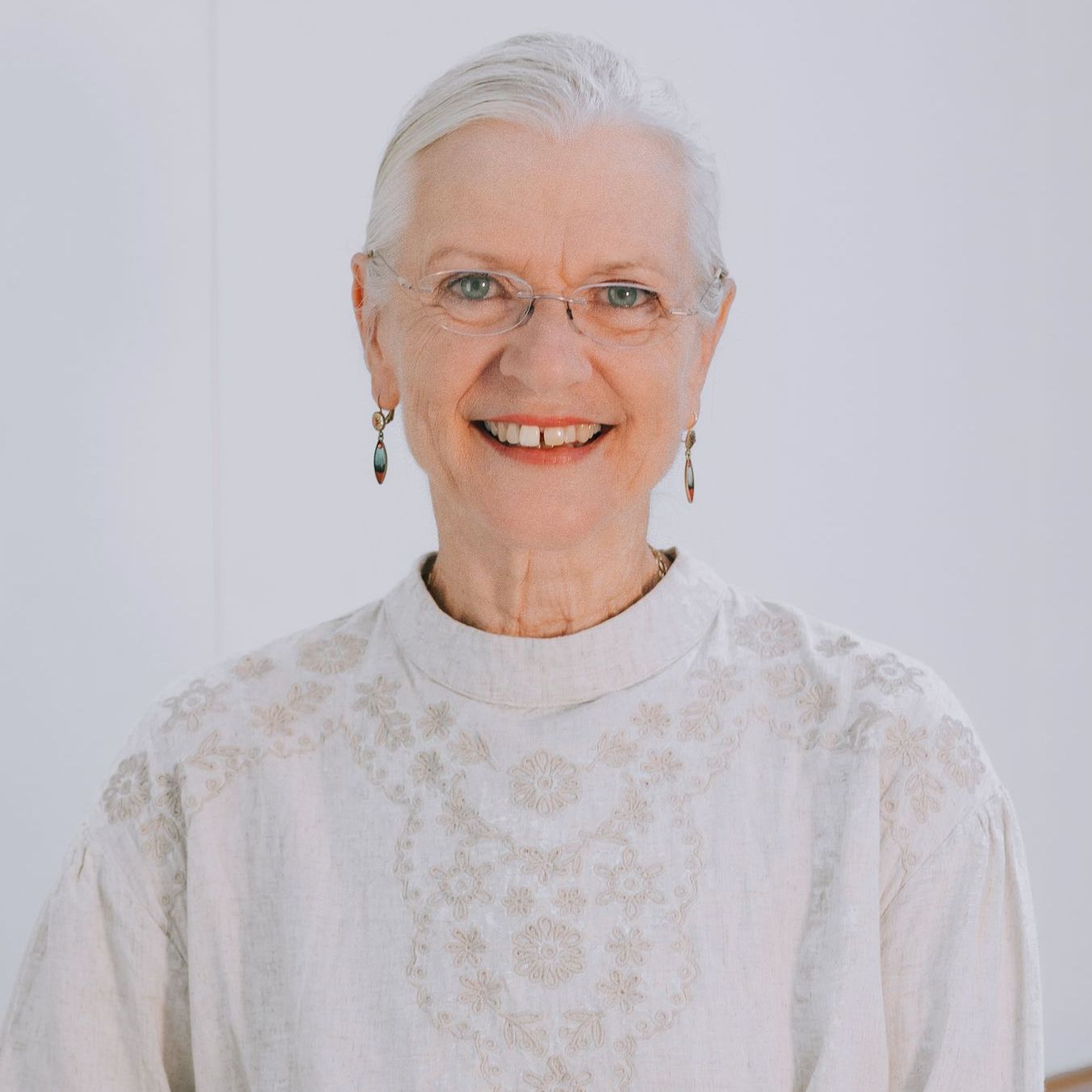 An older woman wearing glasses and a white shirt is smiling for the camera.