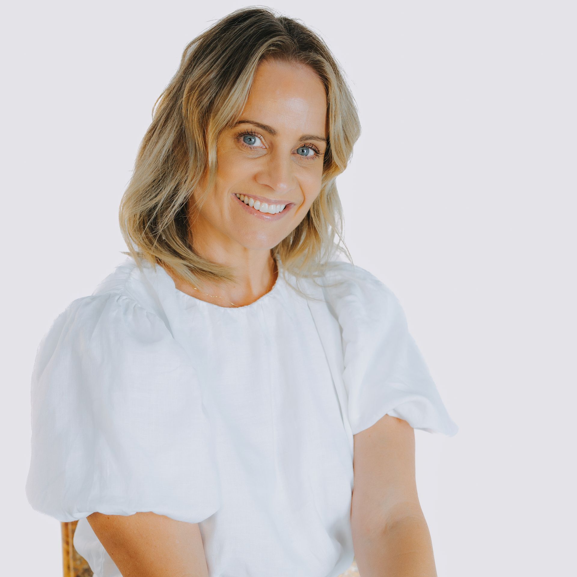 A woman is sitting in a chair wearing a white shirt and smiling.
