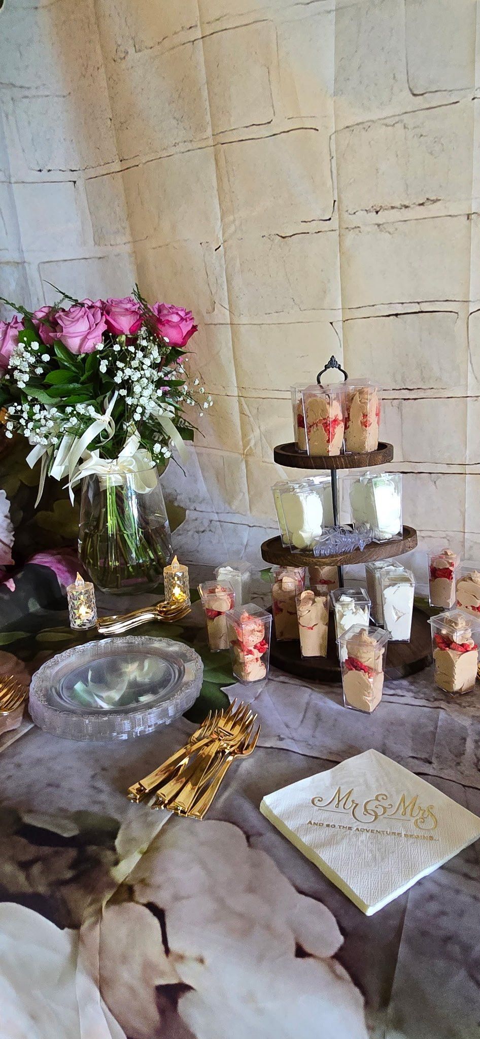 Table setting with pink roses, tiered dessert stand, and favors.