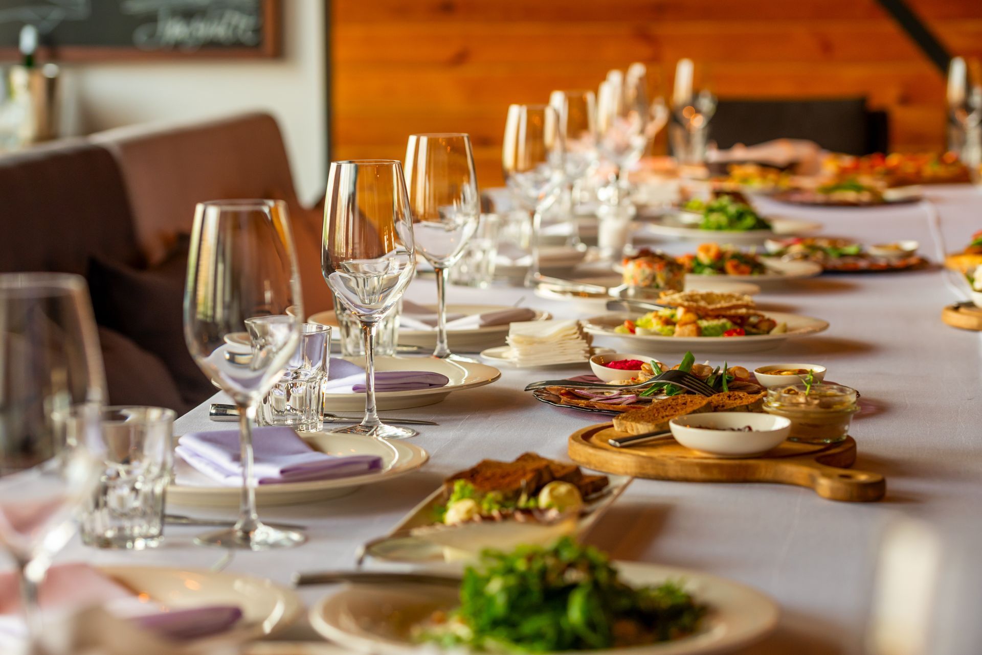 Long table set for a meal with plates of food, glasses, and a white tablecloth.