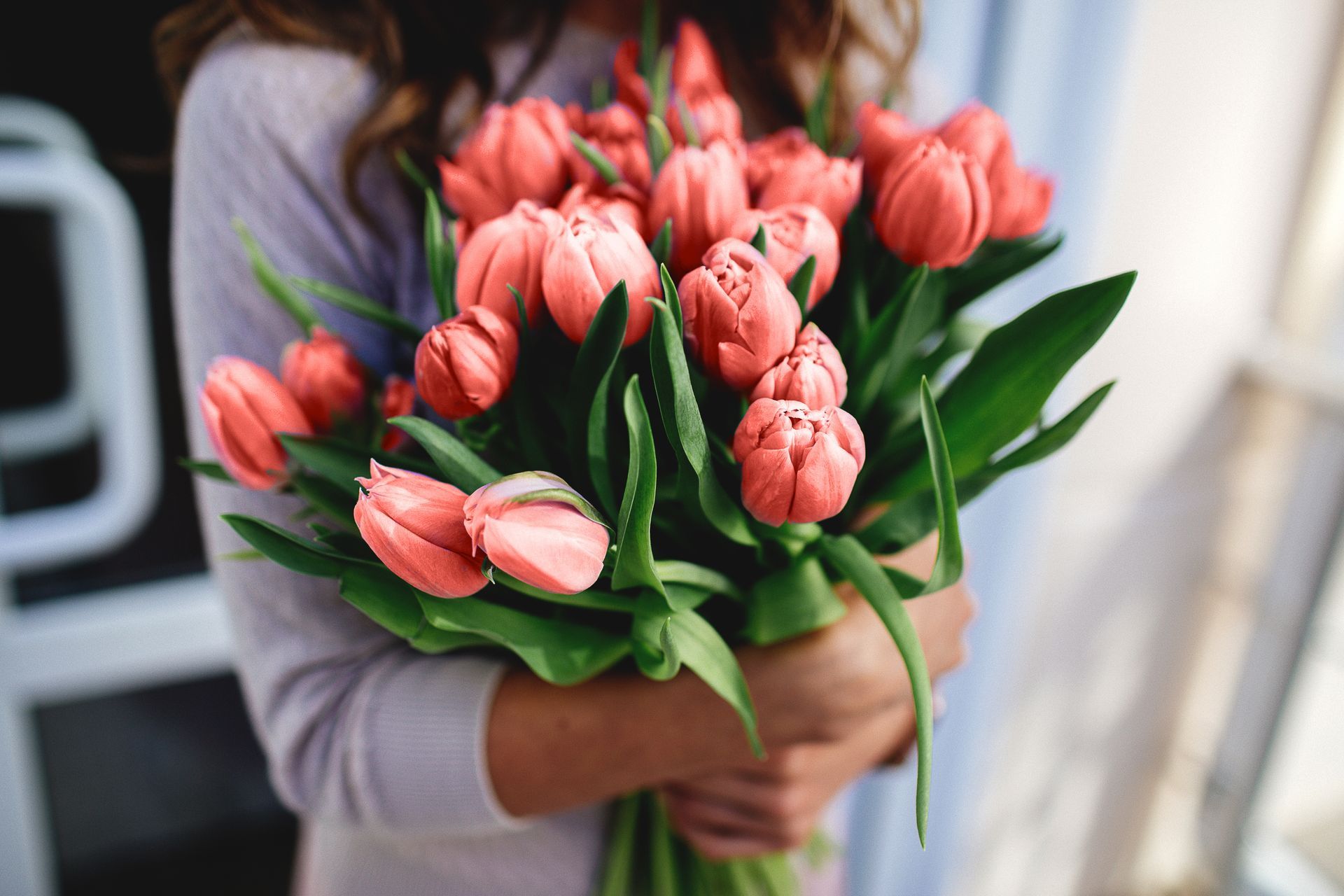 Woman holding a large bouquet of coral-colored tulips.
