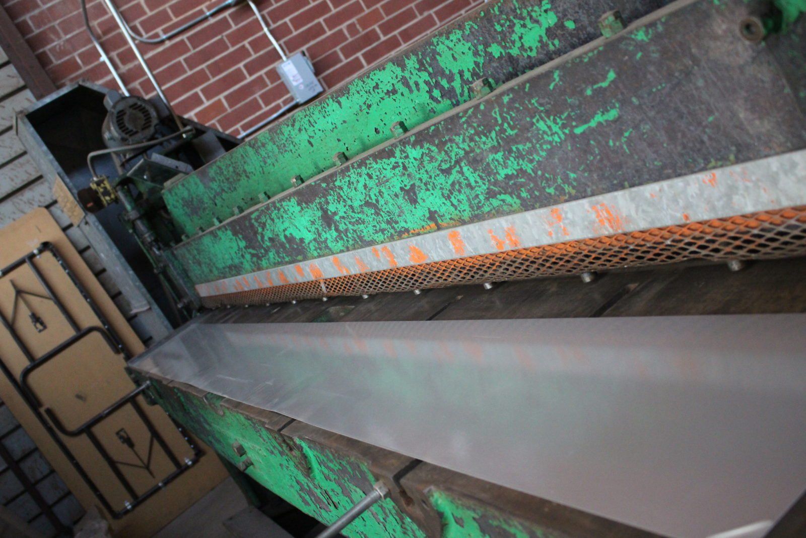 a green machine is cutting a piece of metal