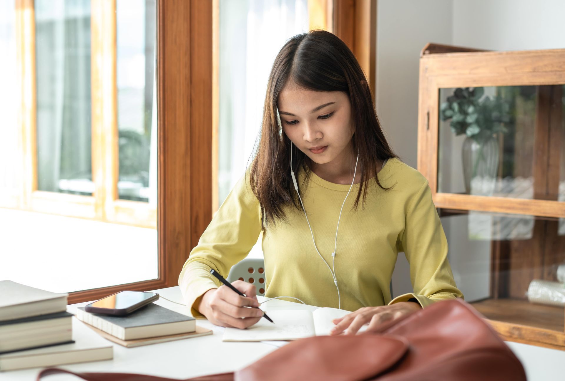 A woman is sitting at a table writing in a notebook.