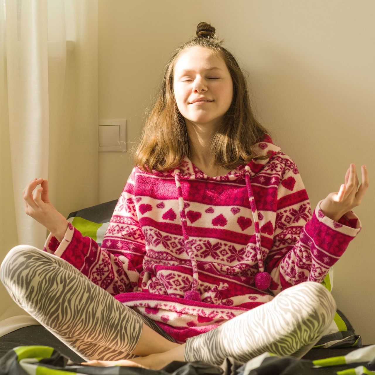 A girl is sitting on a bed with her legs crossed and her eyes closed