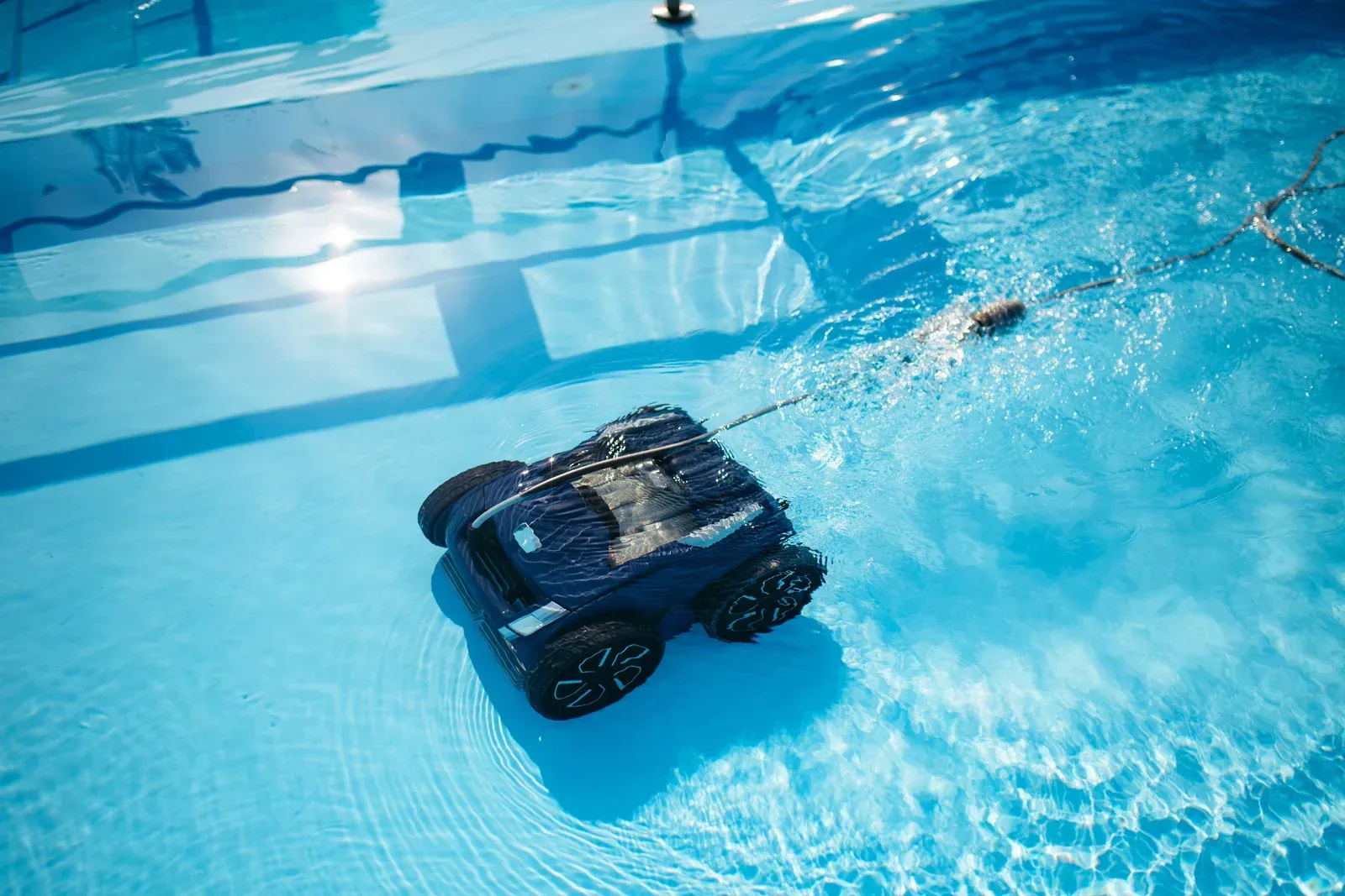 A dark blue robotic pool cleaner moving through clear, blue water in a swimming pool.