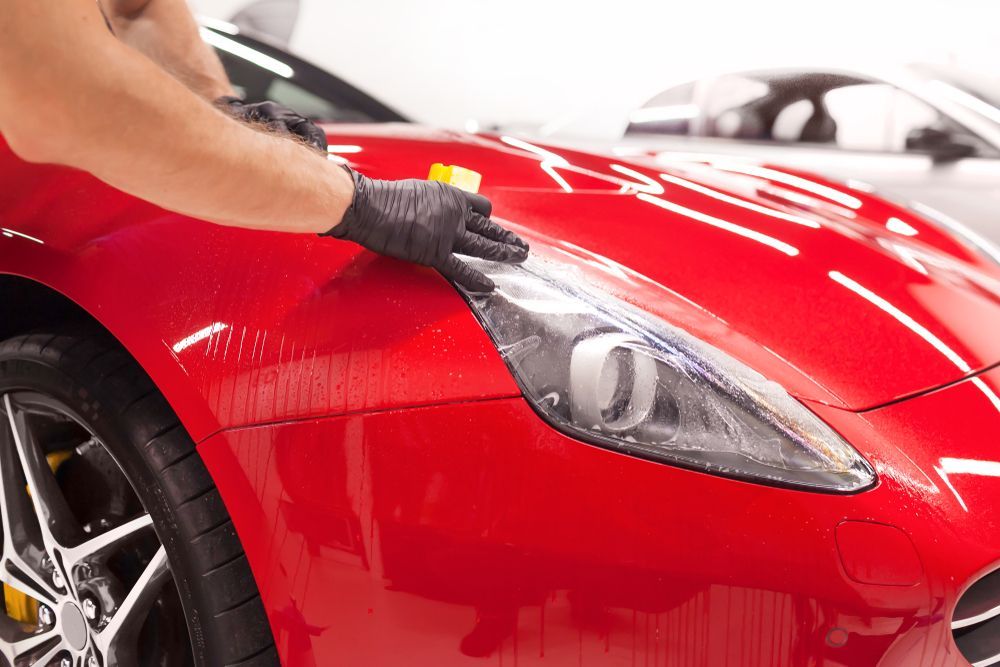 A Person Wearing Black Gloves is Applying PPFto a Red Car's Headlight — Clarence Valley Detailing In Yamba, NSW