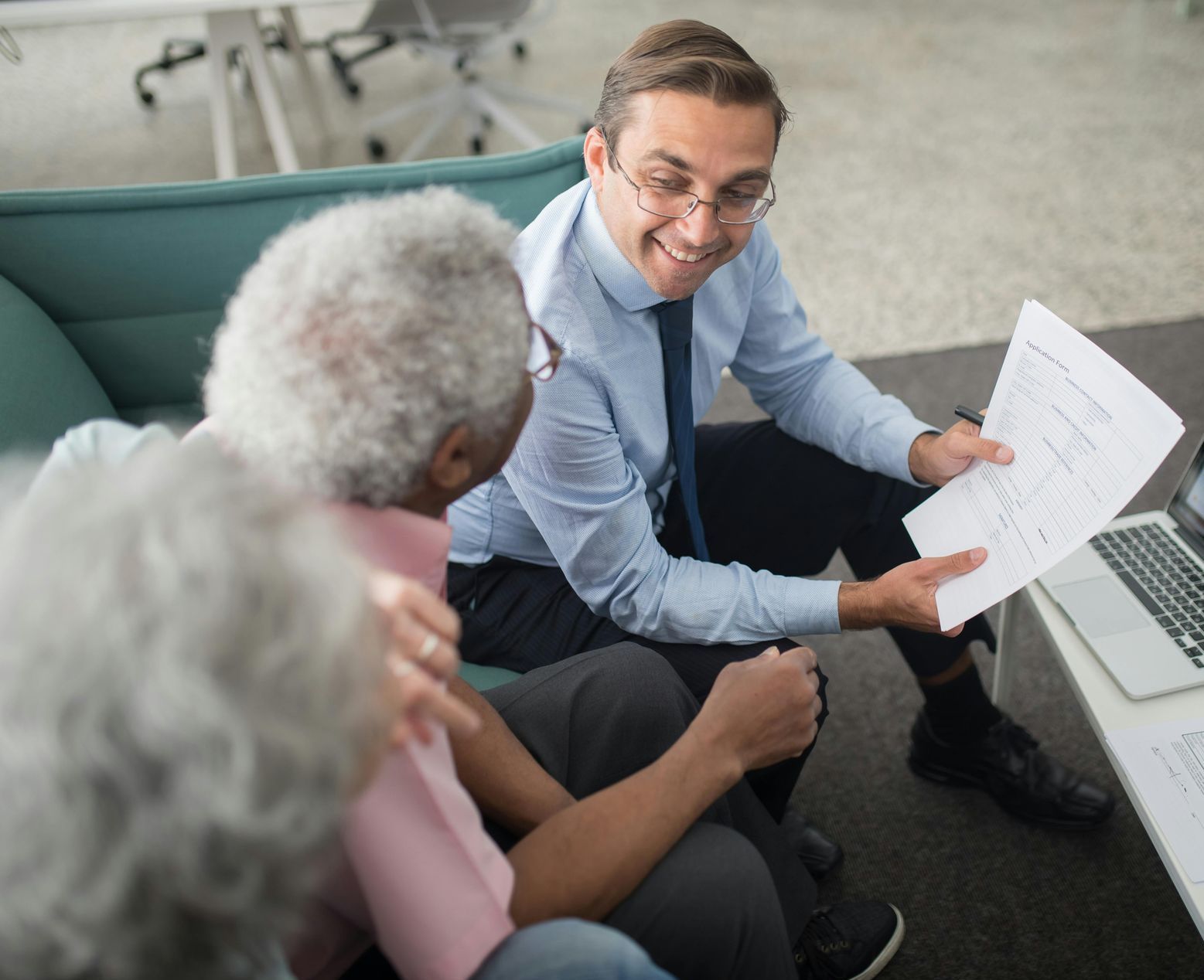 A man is sitting on a couch talking to two older people.